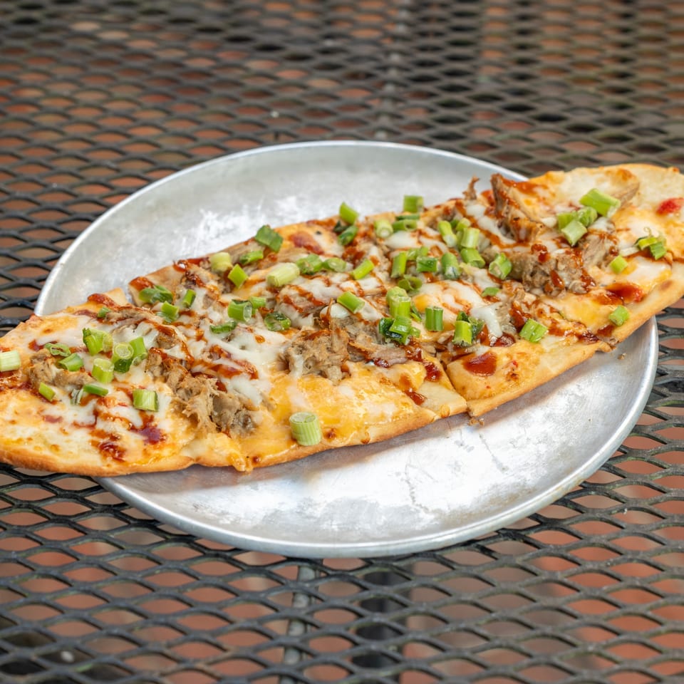 Homegrown Pizza's BBQ chicken flatbread with melted cheese and green onions on a metal tray.