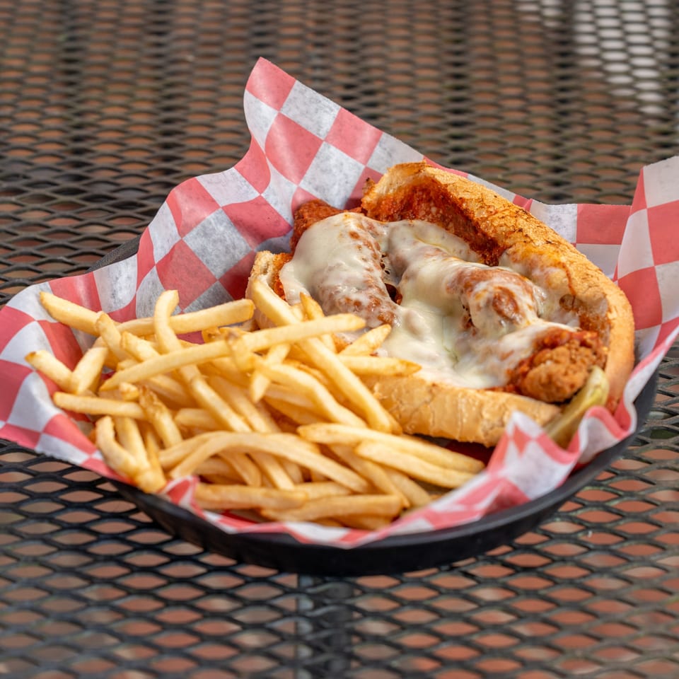 Meatball sub with melted cheese and marinara sauce, served with a side of golden fries.