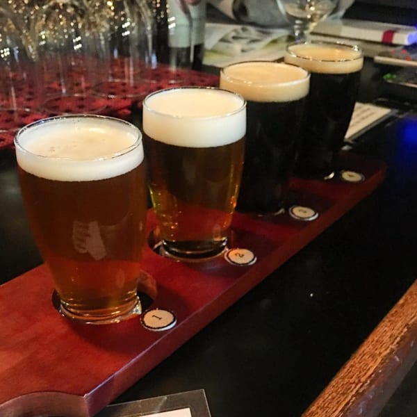 Four beer glasses, two light and two dark, on a wooden tasting paddle at Homegrown Pizza.