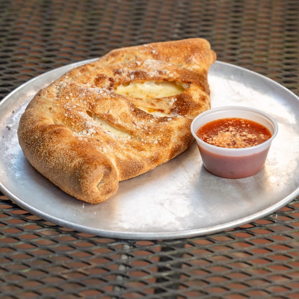 Homegrown Pizza's golden-brown calzone, sprinkled with parmesan, served with a side of marinara sauce.