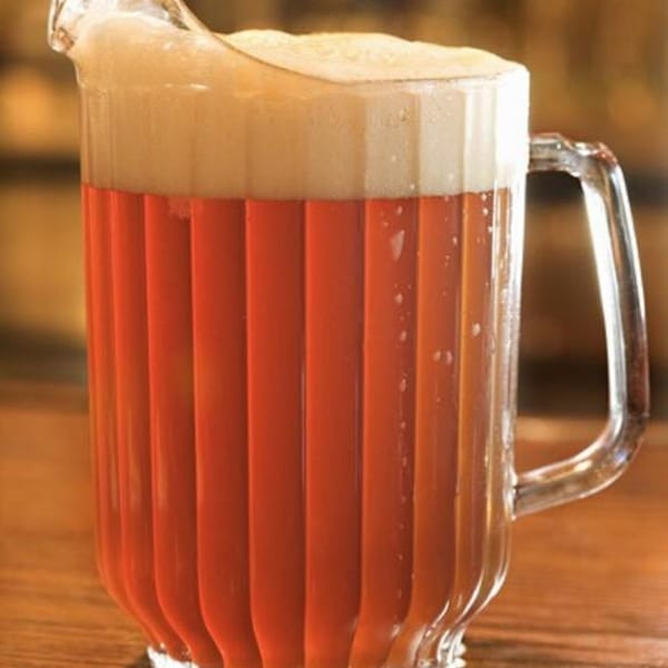 A clear pitcher filled with amber beer and a thick layer of white foam on top.