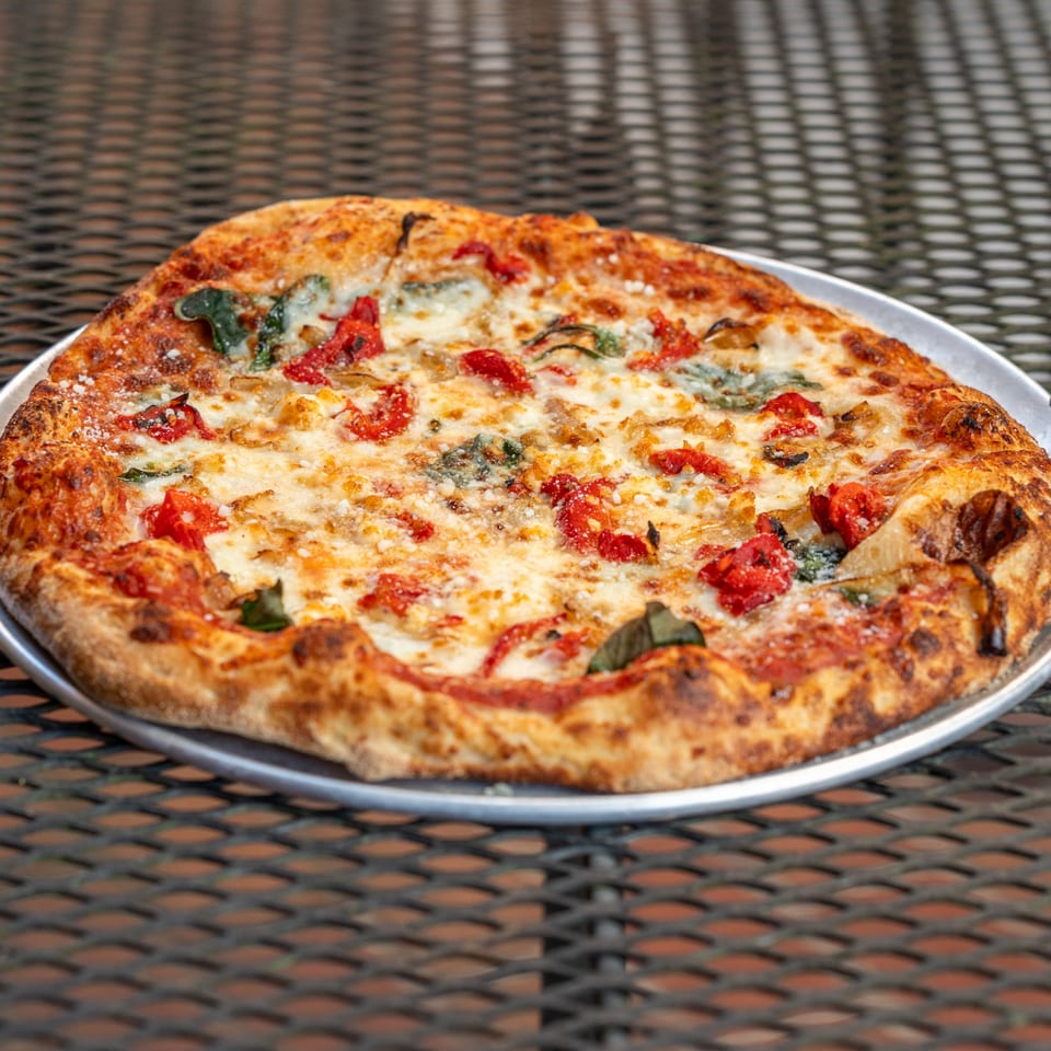 A Homegrown Pizza with melted cheese, red tomatoes, and green basil on a metal tray.