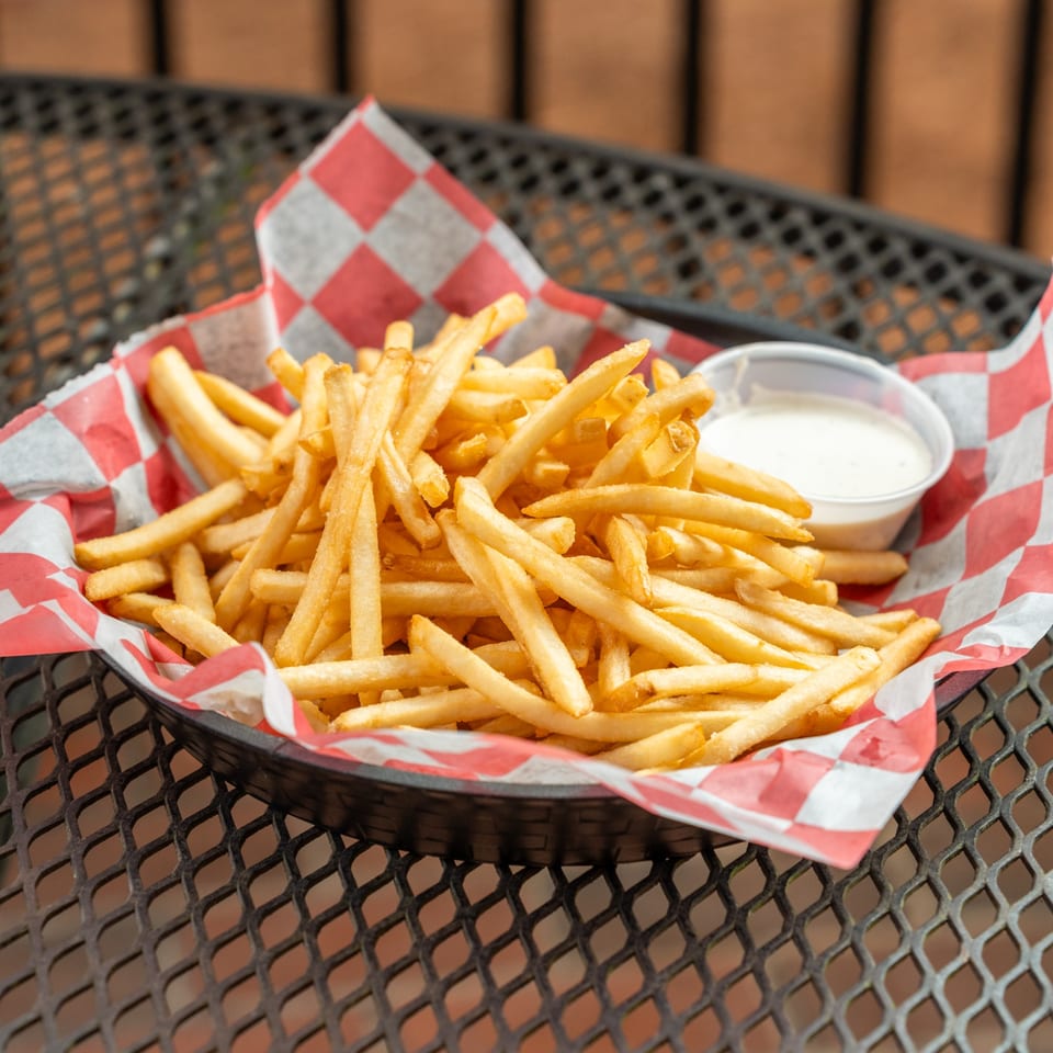 Golden french fries in a red and white checkered paper-lined basket with a side of dipping sauce.