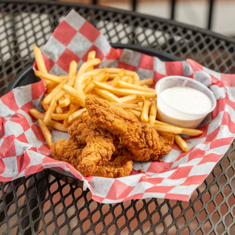 Crispy chicken tenders and golden french fries with a side of dipping sauce in a basket.