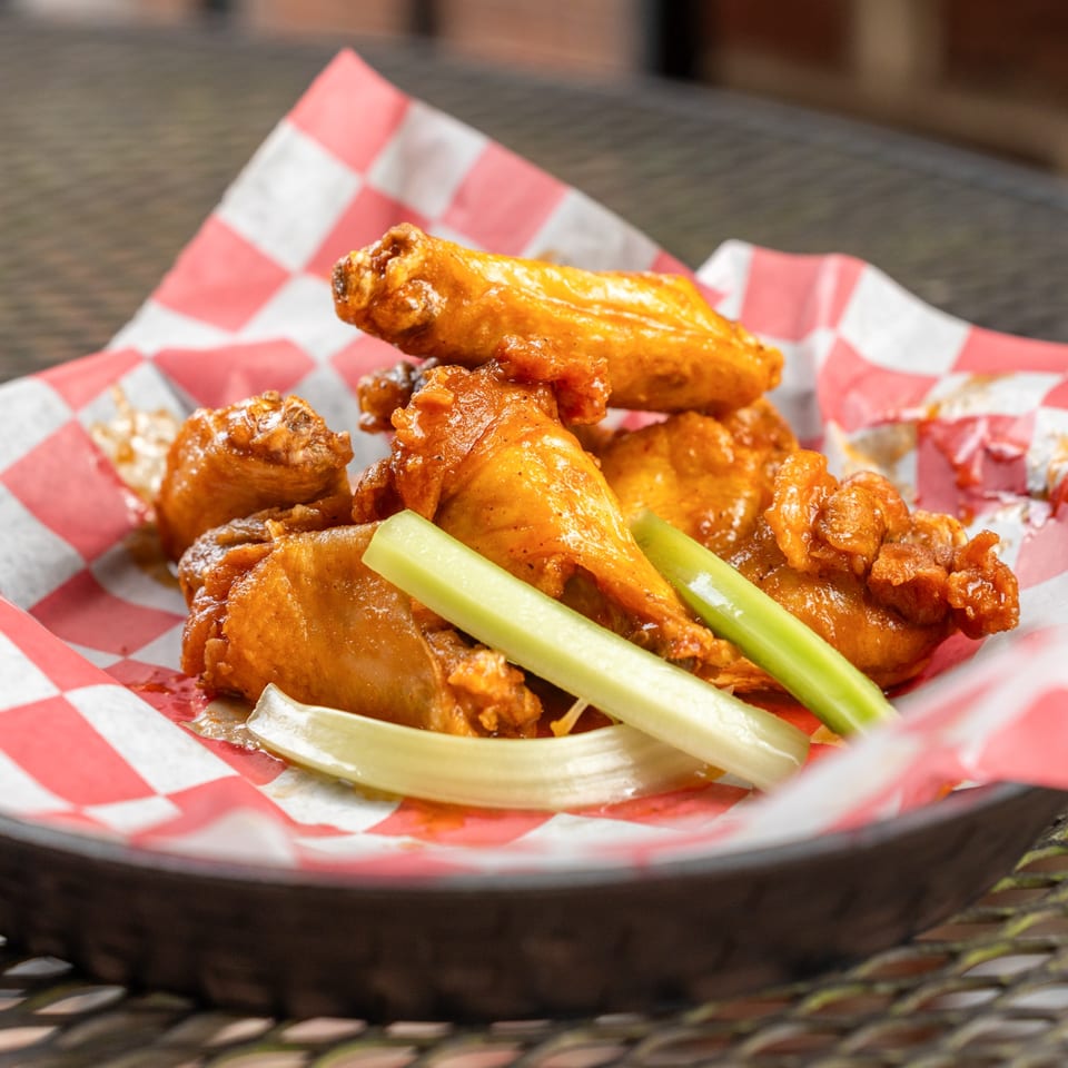 Homegrown Pizza's buffalo wings with celery sticks in a red and white checkered paper-lined basket.