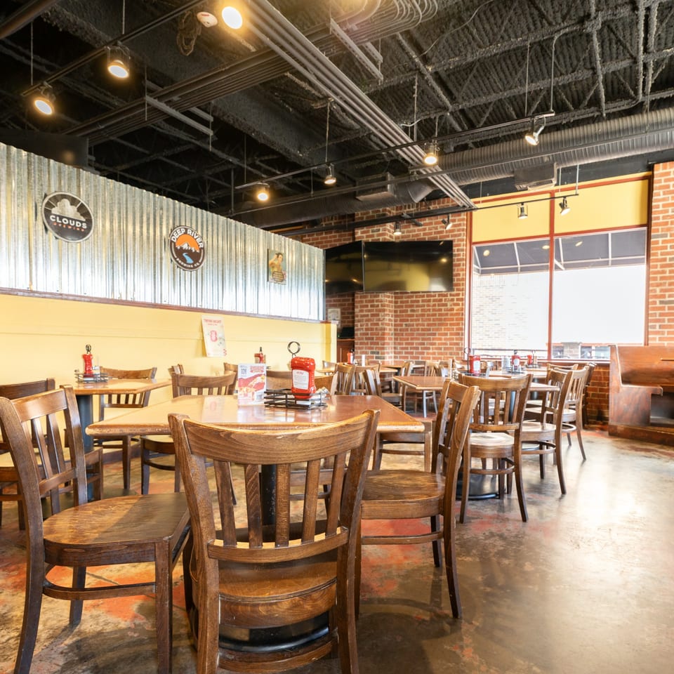 Homegrown Pizza dining room with wooden tables and chairs, exposed brick, and corrugated metal accents.